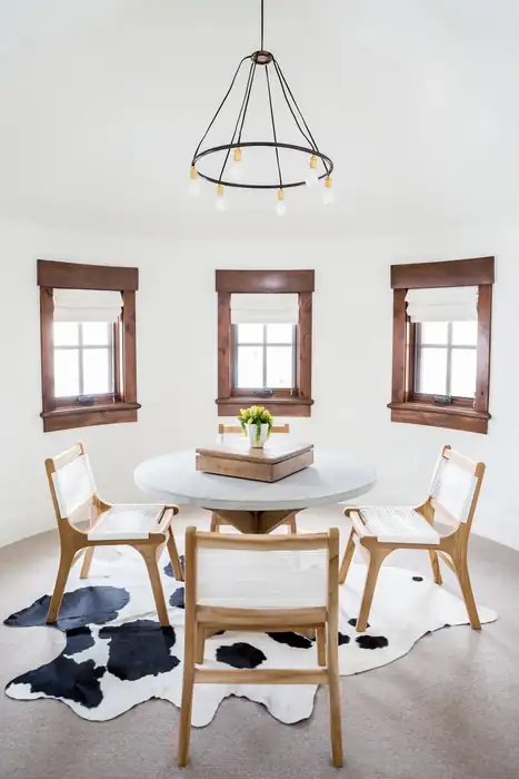 Three white Roman shades around a round dining table.