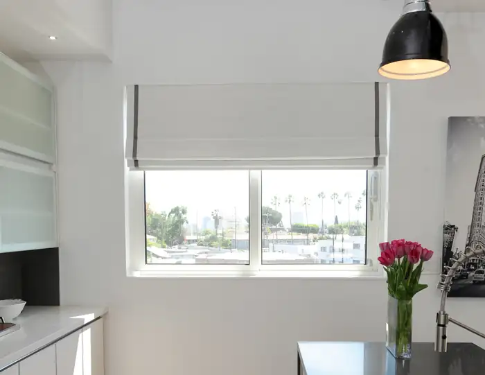 White Roman shade with horizontal folds above a kitchen window