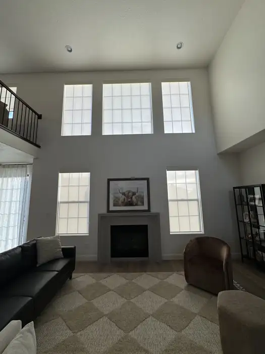 White shades on upper and lower windows around a fireplace in a two-story living room.