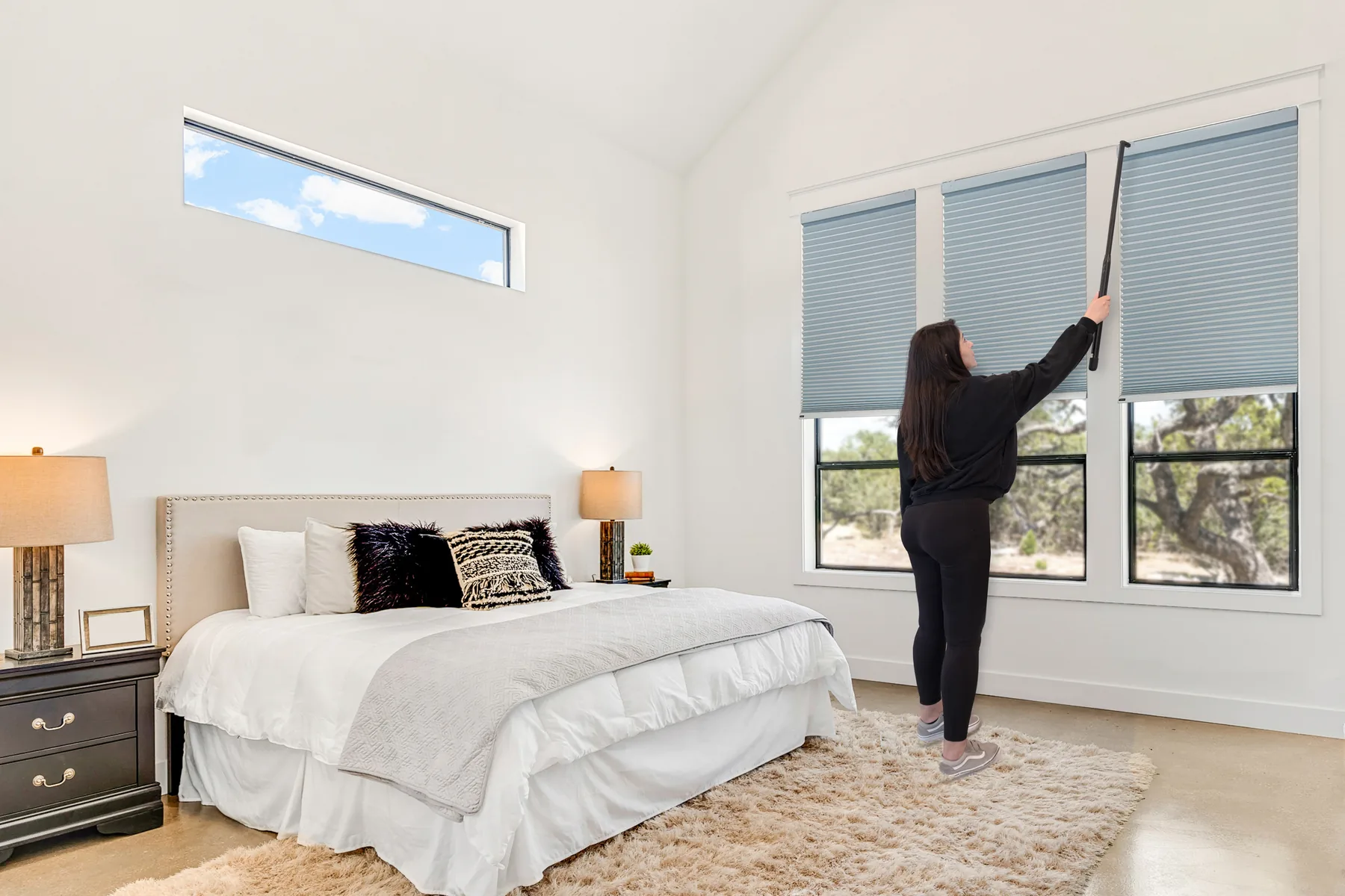 Motorized shades being serviced with a charging wand at a tall bedroom window