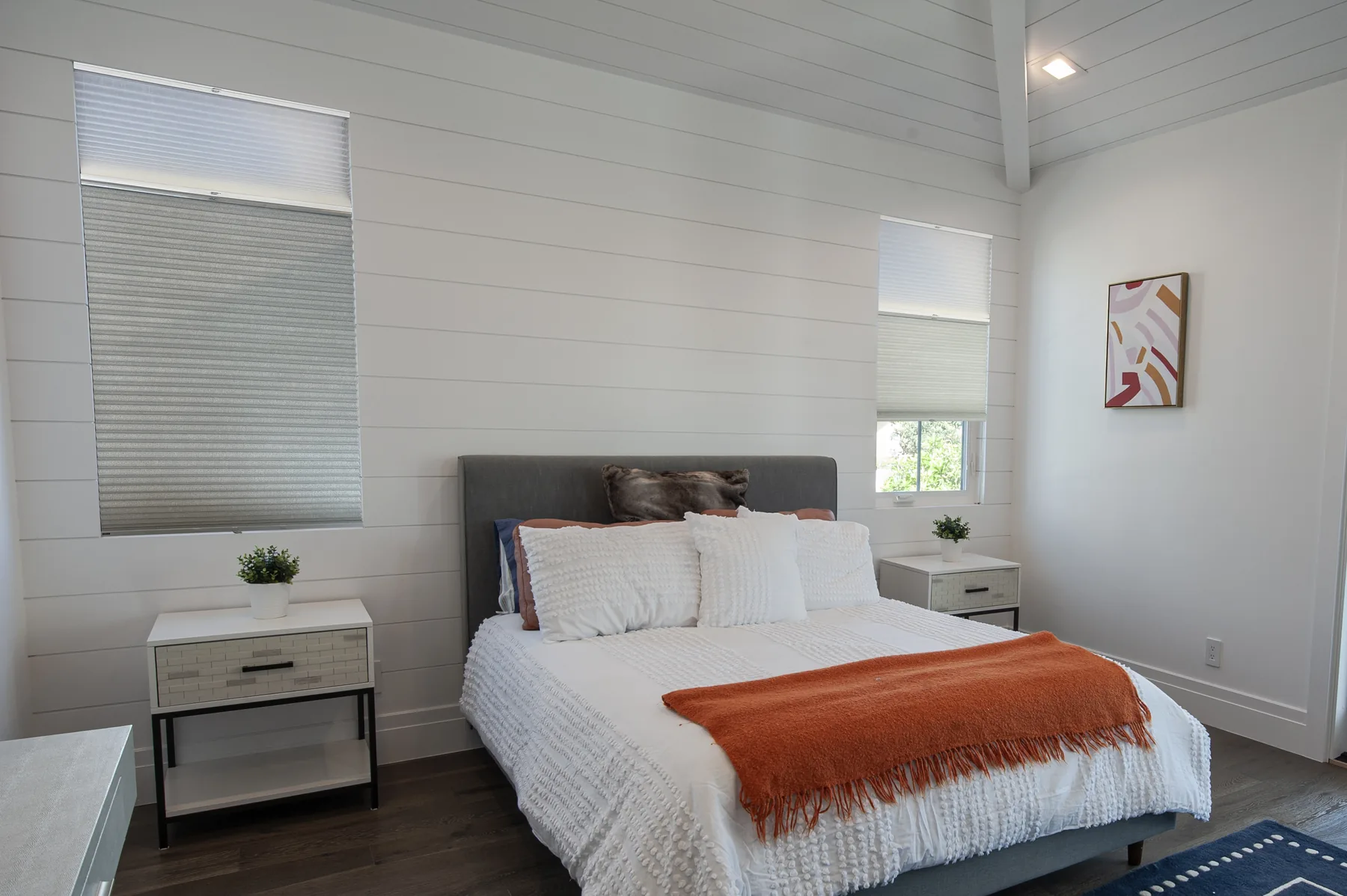 Pleated white shades covering windows beside a bed